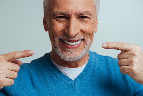 Man with blue sweater pointing to his smile with two hands