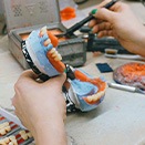 Hands building wax gumline on model teeth for dentures