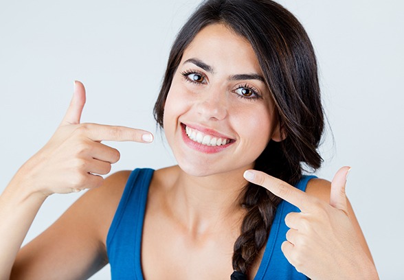 Woman in blue shirt pointing to her smile with both hands