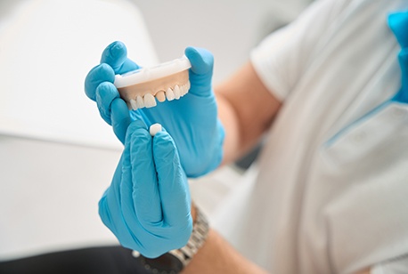 Blue-gloved hands placing sample dental crown over model tooth