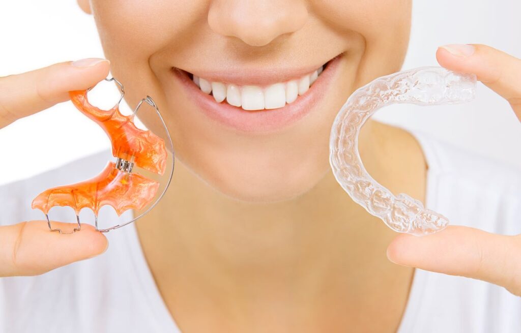 A woman holding a Smart Moves aligner and a retainer.